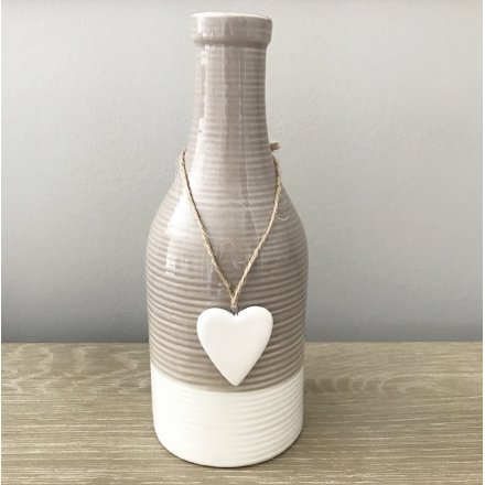 A stylish bottle shaped vase with a glazed finish and a hanging heart decoration.
