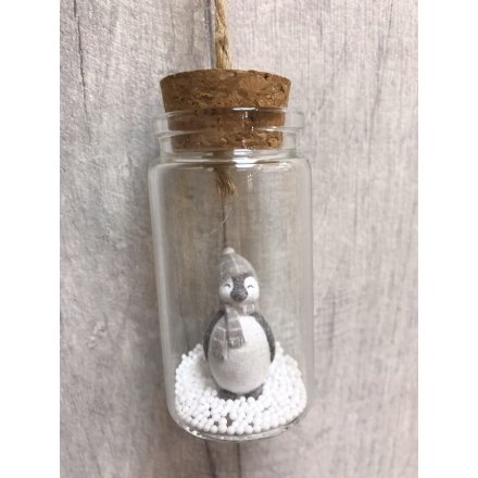 An adorable penguin with a shimmering winter hat and scarf stands upon artificial snow in a glass bottle with cork top.