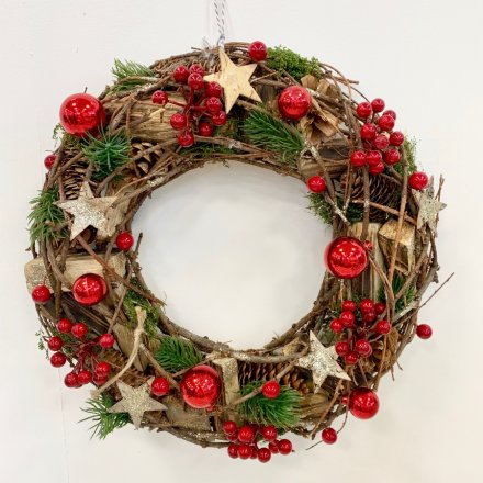  A charmingly clustered Christmas wreath decorated with woodland inspired foliage and scattered with added red accents 