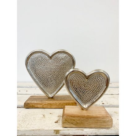 A stylish silver heart ornament with a decorative pattern. Set upon a chunky wooden base making a chic interior item