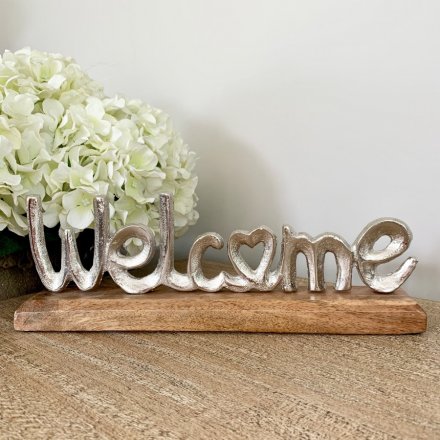 A rough luxe silver welcome sign set upon a chunky wooden base. A chic tabletop decoration for the home.