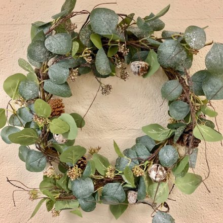 A large round wreath entwined with glittered leaves and decorated with pinecones, bells and berries 