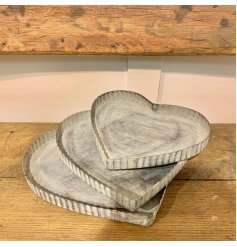 A mix sized set of heart shaped metal trays each decorated with a distressed white washed finish and ridged edge  