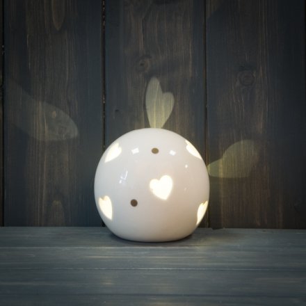 A smooth ceramic ball ornament with a heart cut decal and warm glowing LED centre 