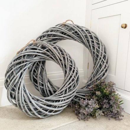 A large woven rattan wreath decorated with a subtle white washed tone and set with a chunky rope hanger 