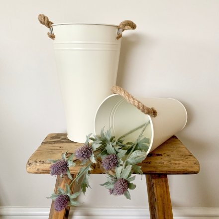 A tall metal bucket in cream with twin chunky rope handles.