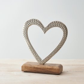 A small aluminium heart ornament placed atop a natural wooden block 