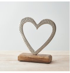 A small aluminium heart ornament placed atop a natural wooden block 