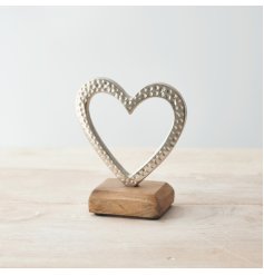 A small aluminium heart ornament with a silver tone and hammered effect, placed atop a natural wooden block 
