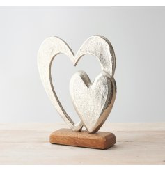 A small double aluminium heart ornament placed atop a natural wooden block 