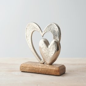 A small double aluminium heart ornament placed atop a natural wooden block 