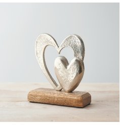 A small double aluminium heart ornament placed atop a natural wooden block 