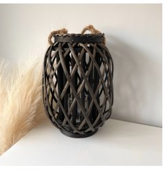  A dark toned woven wicker lantern with a chunky rope handle accent and glass insert 