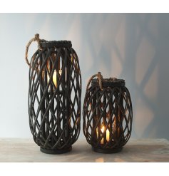 A dark toned woven wicker lantern with a chunky rope handle accent and glass insert 