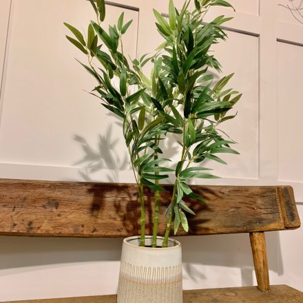 A tall standing artificial bamboo stalk potted in a simple back base 