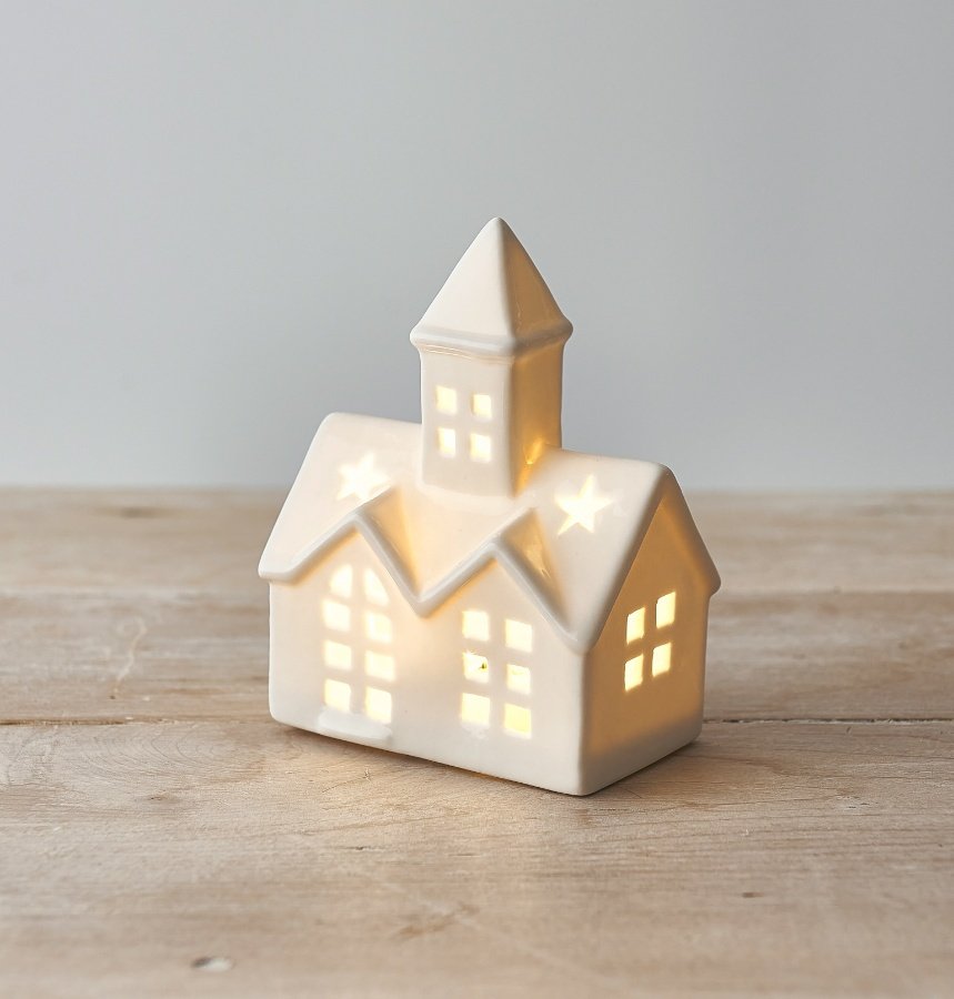 A small ceramic church inspired decoration, set with a high pointed steeple, white tone and warm led light from inside