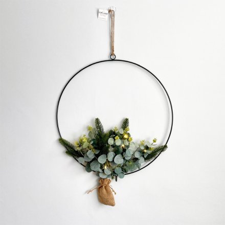A simple metal hoop wreath entwined with green leaf foliage and added warm glowing LED lights  