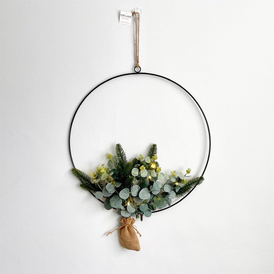  A charmingly simple hanging hoop wreath with entwined greenery leaves and added warm white lights 