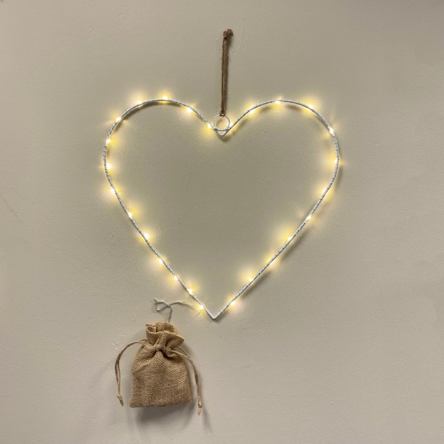 A white metal wire heart decoration with warm glowing LED lights and a hessian battery bag 