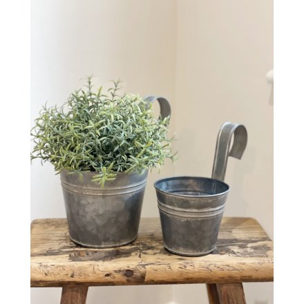 An aged looking metal planter featuring a curved handle, perfect for hanging on fences and balconies 