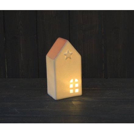 A small ceramic house with white tones and a blush pink roof complete with a warm glowing LED central light and star emb