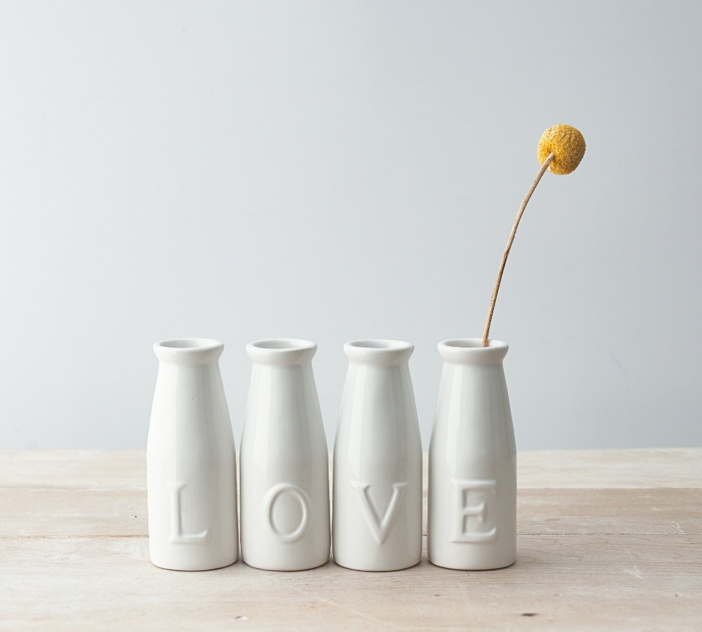 A set of simple white toned ceramic milk bottles, each embossed with a letter that spells out LOVE 