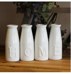 A set of simple white toned ceramic milk bottles, each embossed with a letter that spells out HOME 