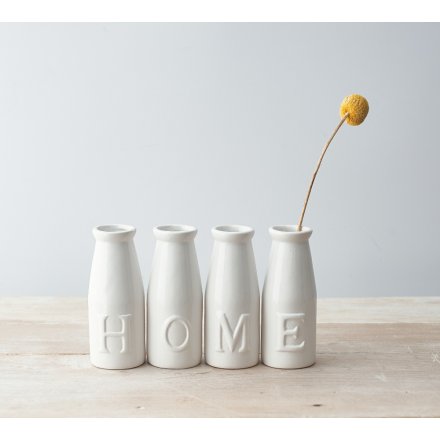 A set of simple white toned ceramic milk bottles, each embossed with a letter that spells out HOME 