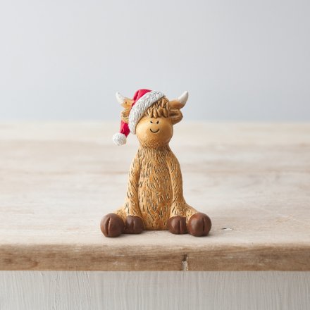A cute sitting highland cow ornament with a cute smiling face and a santa hat.