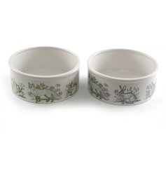 An assortment of 2 ceramic pet bowls, each with a stylish forest toile design in earthy green and ink blue hues. 