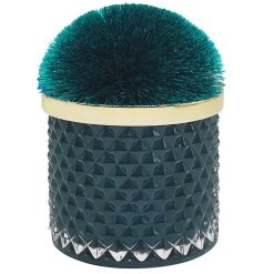 A luxury scented candle set within a jewel coloured glass pot with a pom pom lid.