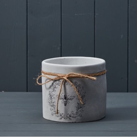 A unique plant pot with a white textured finish and charming bee and wreath design. Complete with jute string bow.