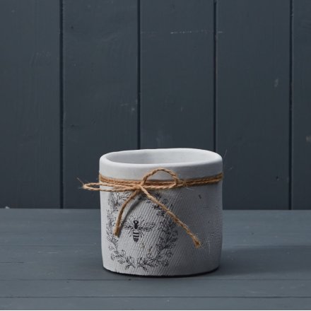 A rustic plant pot with a white textured surface and a charming bee and wreath design. Complete with a rustic jute bow. 