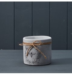 A rustic plant pot with a white textured surface and a charming bee and wreath design. Complete with a rustic jute bow. 