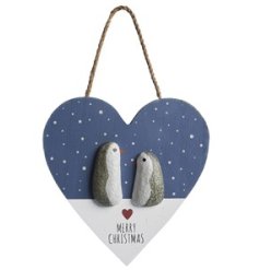 A cute blue and white wooden hanging sign in a heart shape with pebble penguin detail and "Merry Christmas" message. 