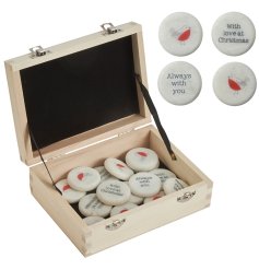 A natural wooden chest containing an assortment of small marble pebbles, each decorated with a festive message or design