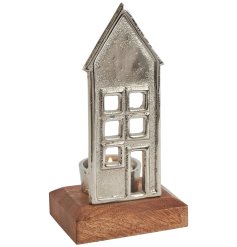 A beautiful silver metal house with cut out windows and door detail and tea light holder on a wooden base. 