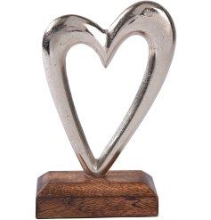 A beautiful silver metal heart with a cut out design on a contrasting wooden base. 