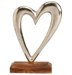A beautiful silver metal heart with cut out detail on a contrasting wooden base. 