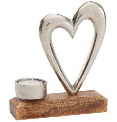 A beautiful silver metal shaped heart silhouette alongside a matching metal tea light holder on a wooden base. 