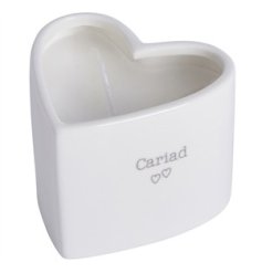 A pretty heart shaped candle with a clean white aesthetic, heart detail and "Love" message in Welsh. 
