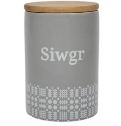 A pretty kitchen canister with "Sugar" written in Welsh on a grey background with white blanket stitch pattern. 