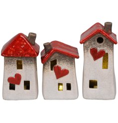 An assortment of 3 stone house led decorations, each with crooked design, cut out windows, and red heart details.