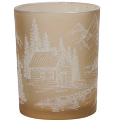 A fawn coloured glass tea light holder with a Winter inspired mountain scene design complete with log cabin detail.