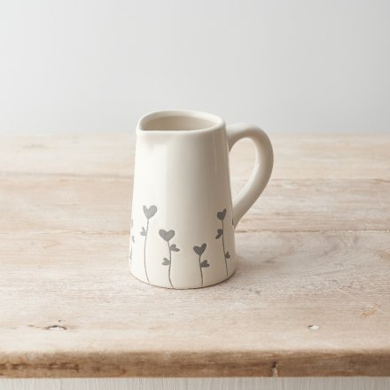 A rustic jug with a grey floral and heart design. 