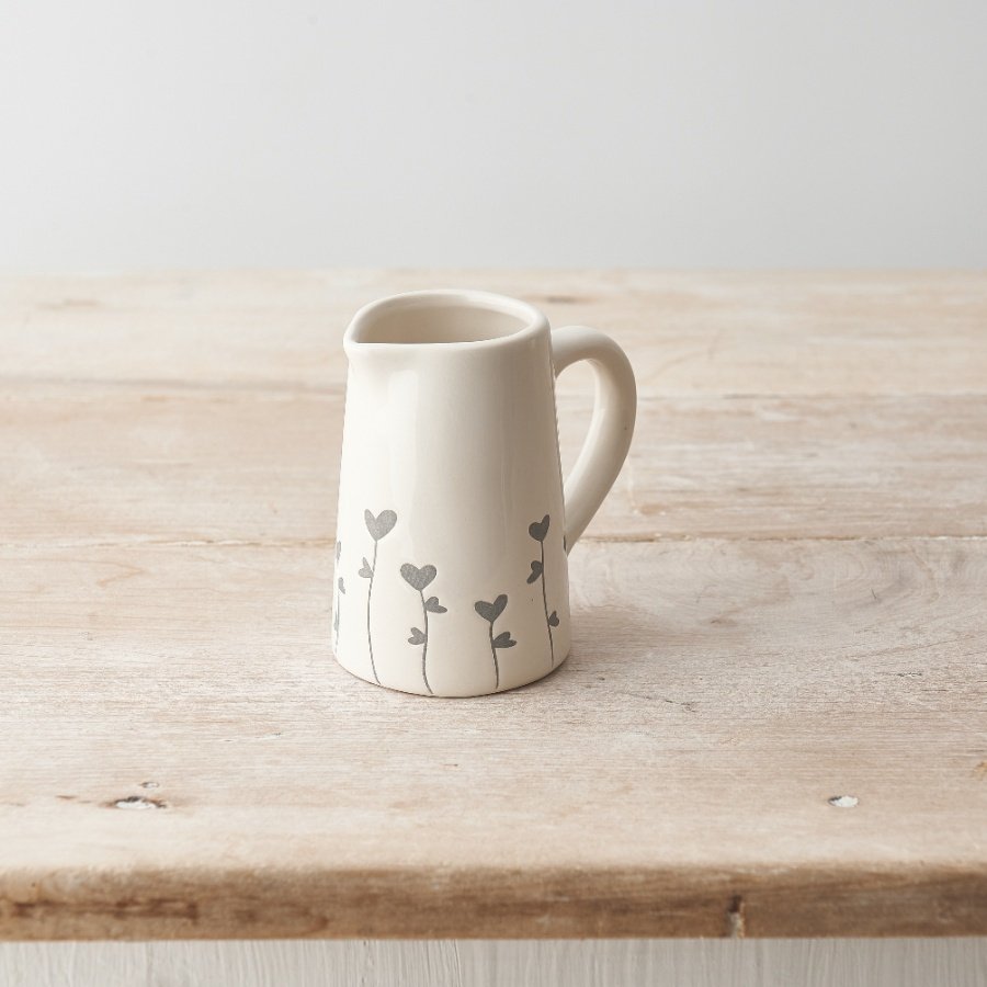 A dainty ceramic jug with a dainty floral and heart design wrapped around the base. 