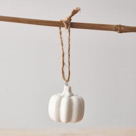 A dainty white ceramic pumpkin with a glossy finish and jute string hanger. 