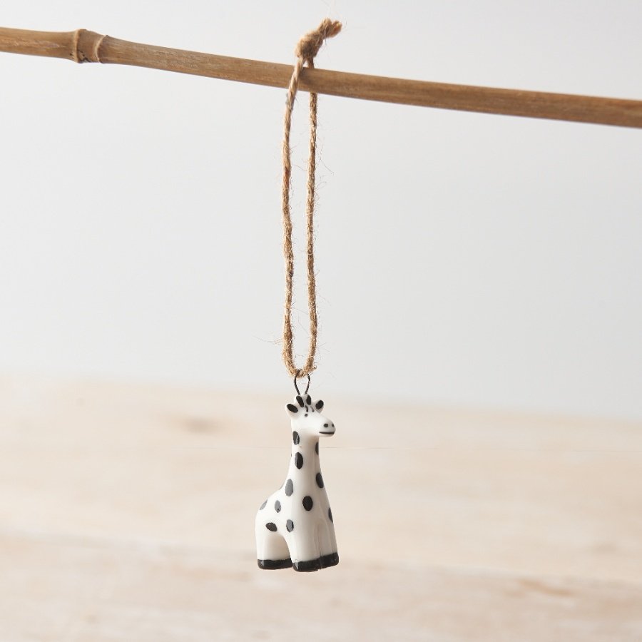 A decorative hanging porcelain giraffe with a twine hanger and spotted monochrome design. 