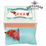 An adorable little sausage dog soft toy in a striped jumper with polka dot bed presented in an illustrated box. 