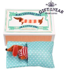 An adorable little sausage dog soft toy in a striped jumper with polka dot bed presented in an illustrated box. 